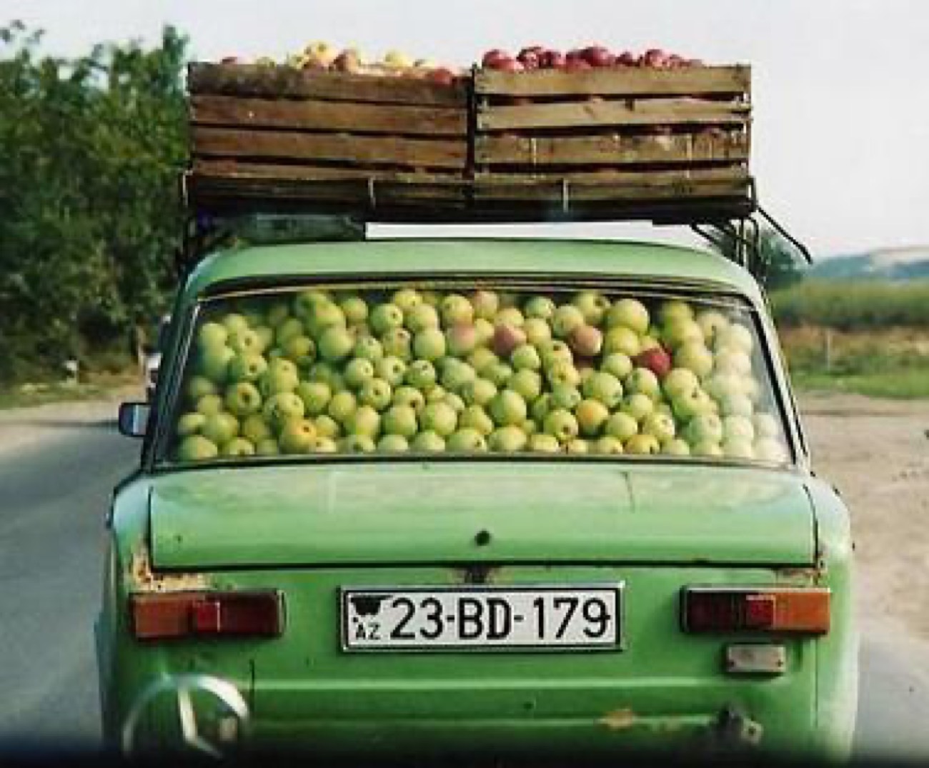 A green car loaded with crates of apples