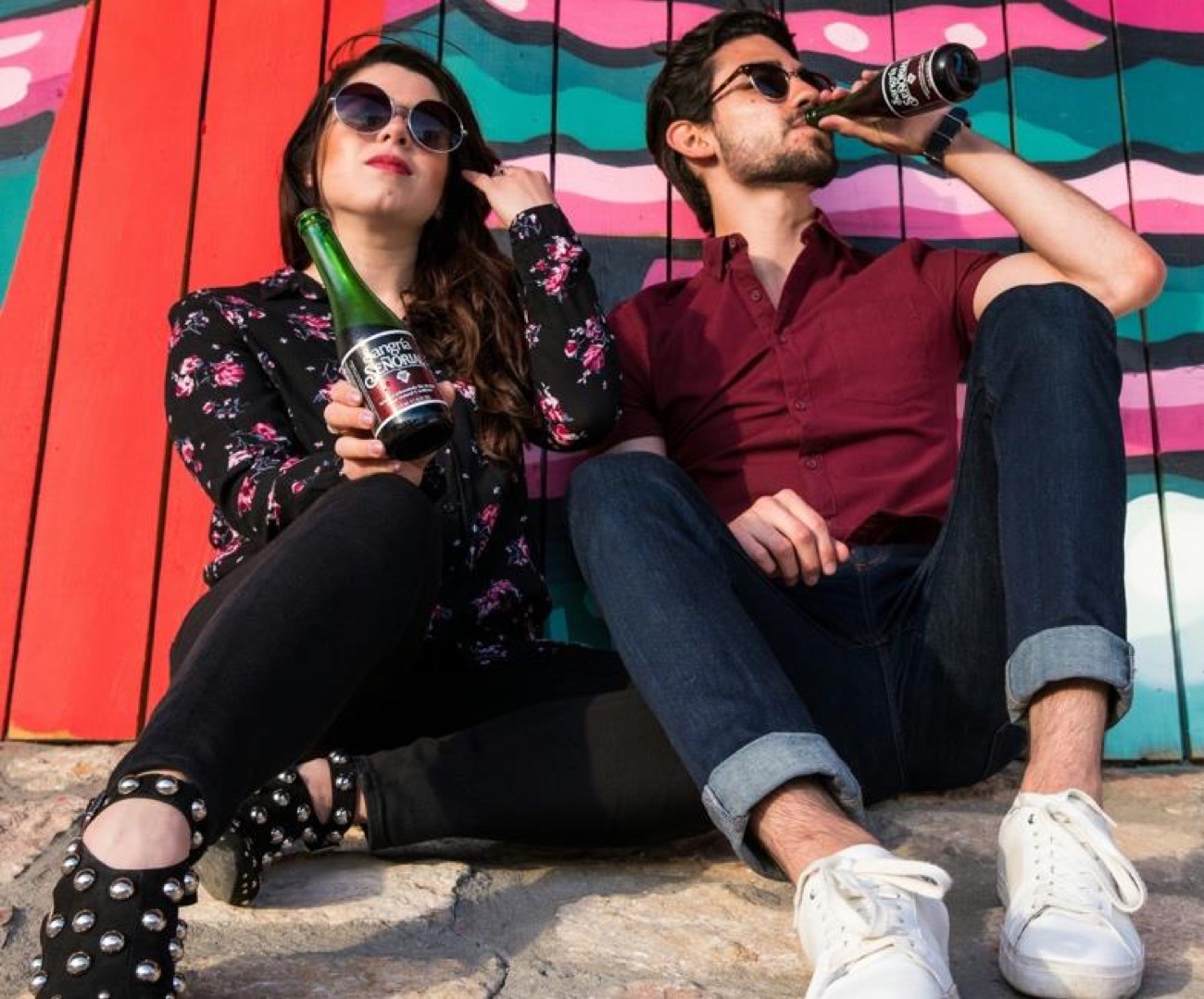 Two friends drinking beers against a painted wall