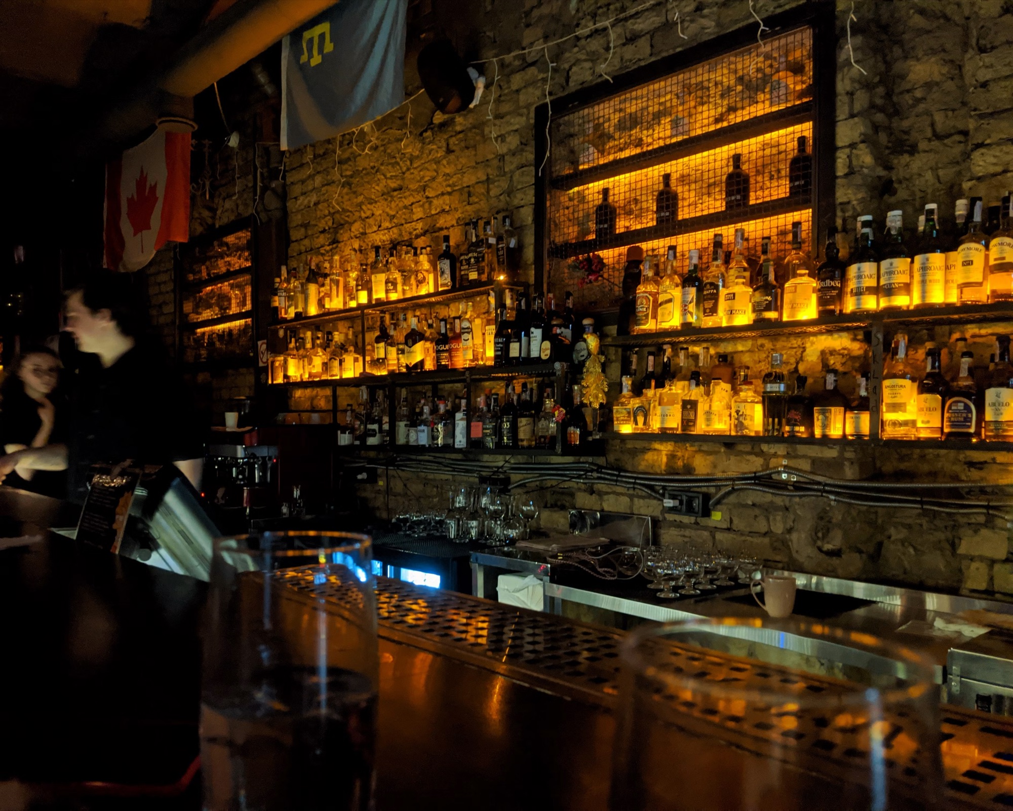 Backlit bottles on raw brick behind a dark bar